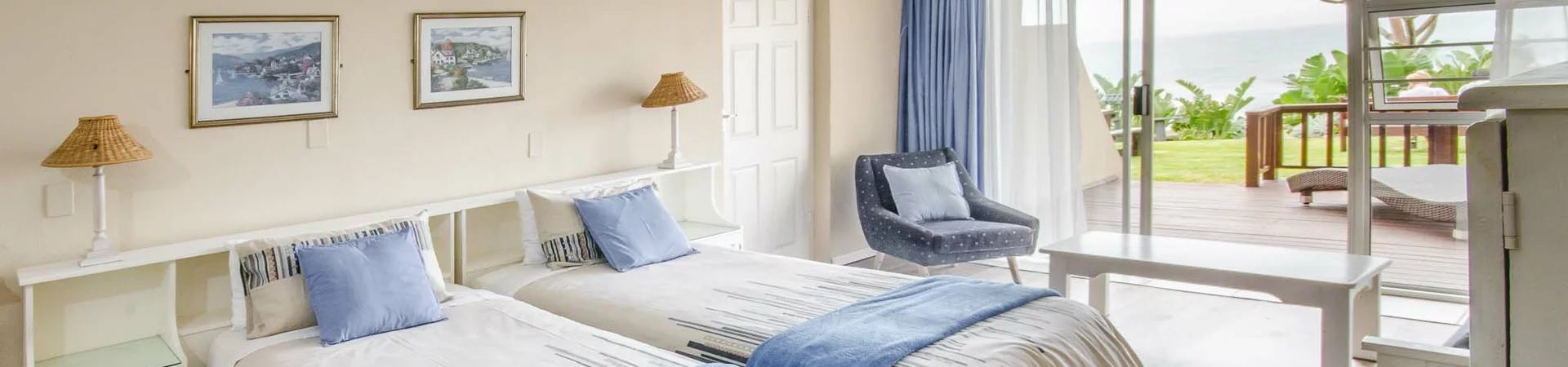 A cozy beachside hotel room featuring two twin beds, light decor, and a view of the ocean.